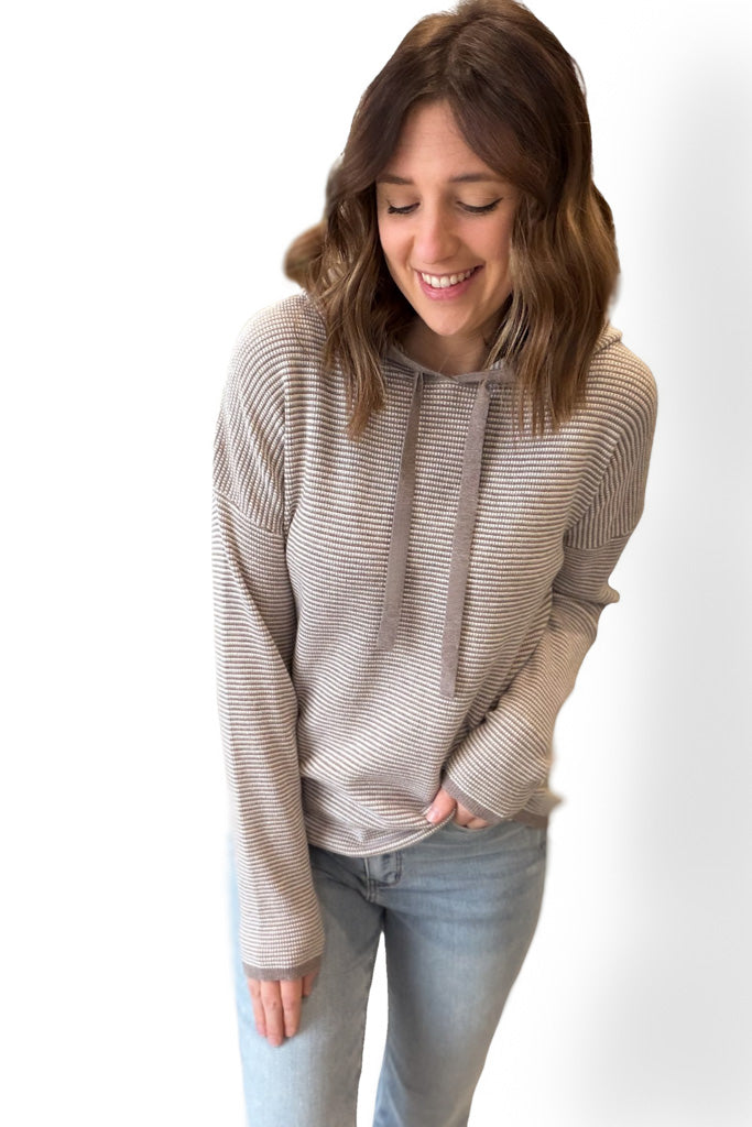 Woman wearing a mocha striped hoodie and light blue jeans on a white background