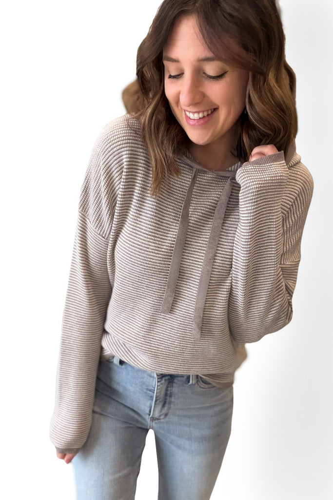Woman wearing a mocha pullover and light blue jeans on a white background