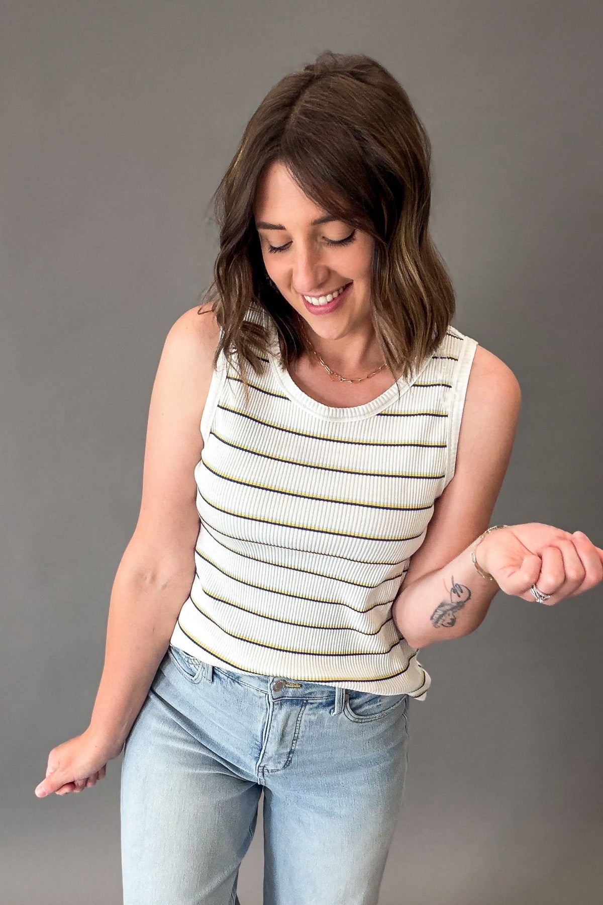 Woman wearing a striped sleeveless top and jeans against a gray background