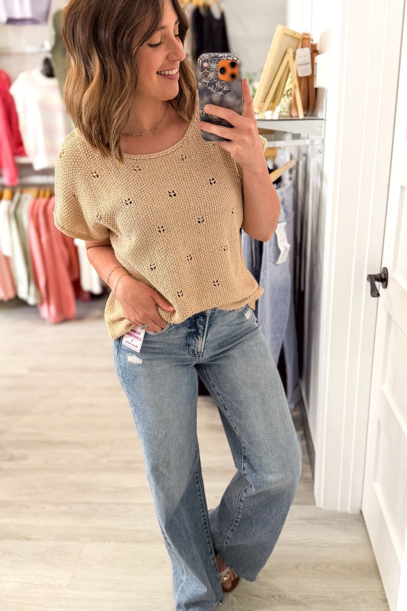 Woman taking a mirror selfie wearing a natural knitted sweater and blue jeans in a clothing store.