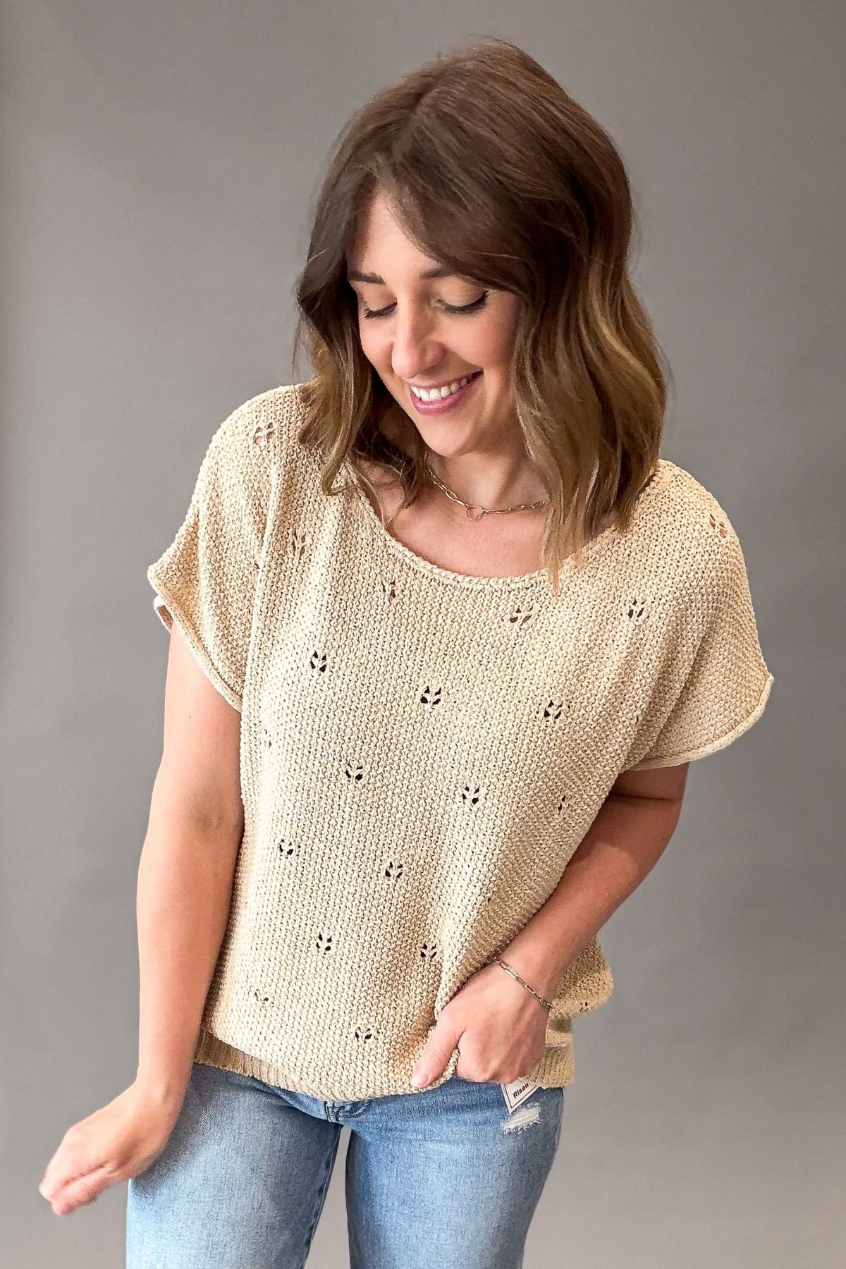 Woman wearing a natural knitted top with a subtle pattern against a gray background