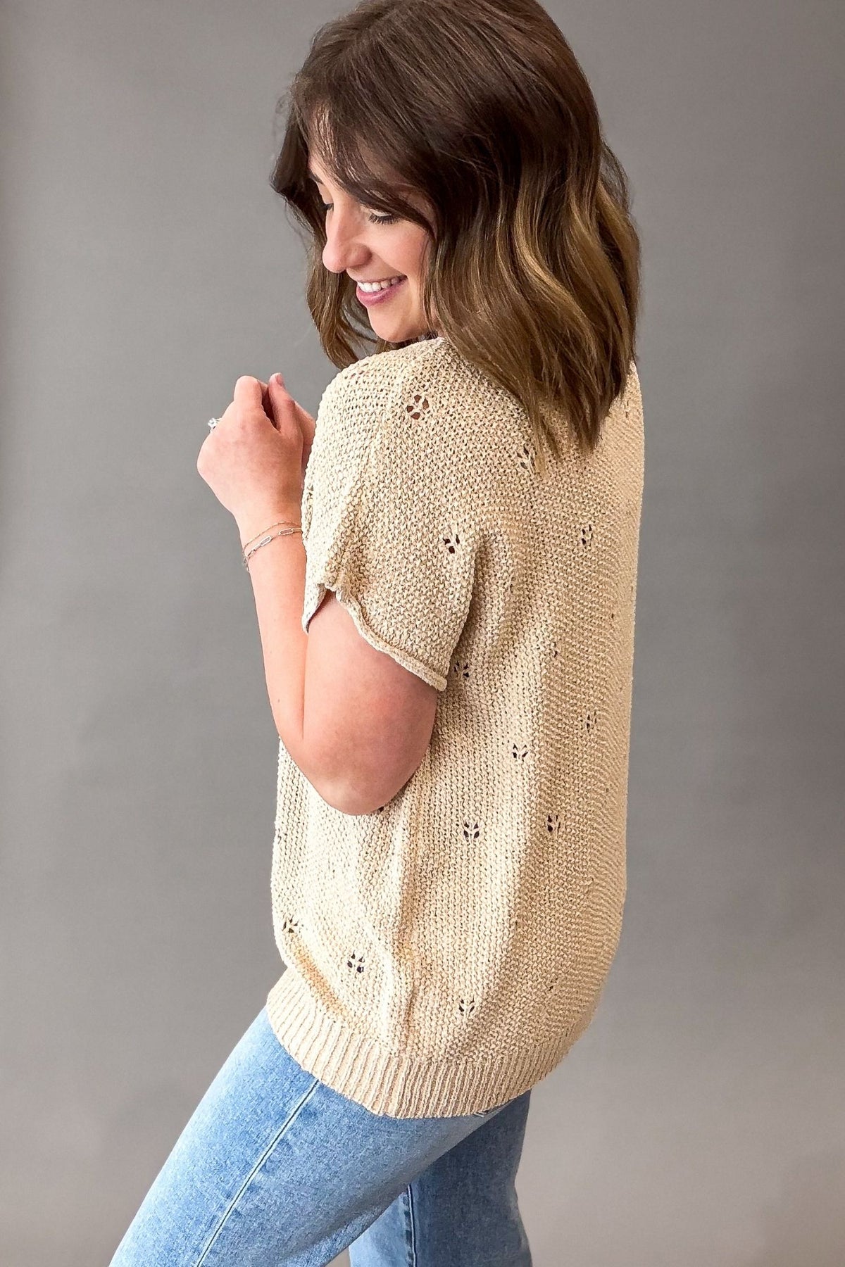 Woman wearing a natural knitted sweater with a subtle pattern on a plain background
