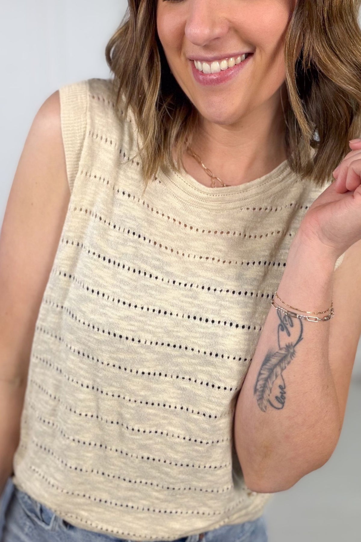 Woman wearing a beige sleeveless top with a subtle pattern against a plain background showing pointelle texture details