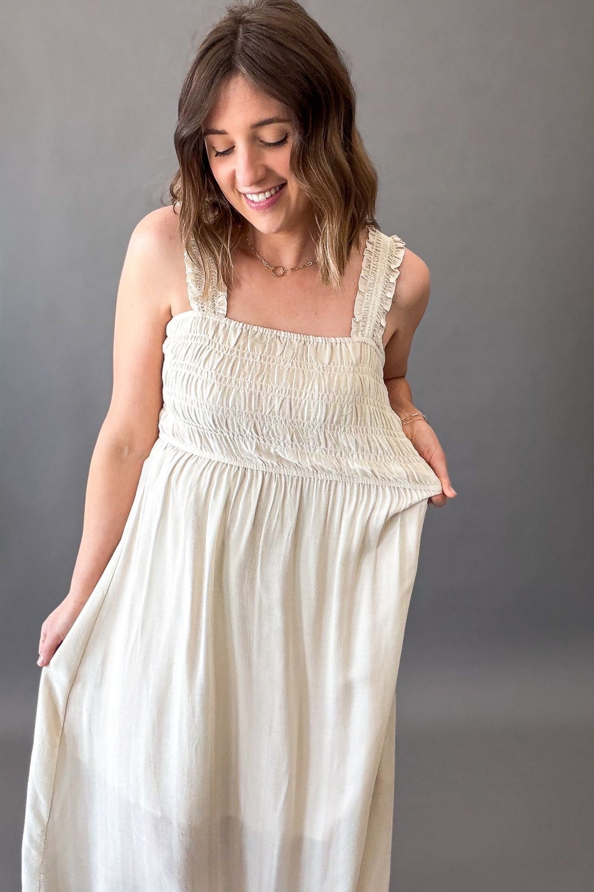 woman wearing a natural smocked sleeveless midi dress showing stretch in the waistband