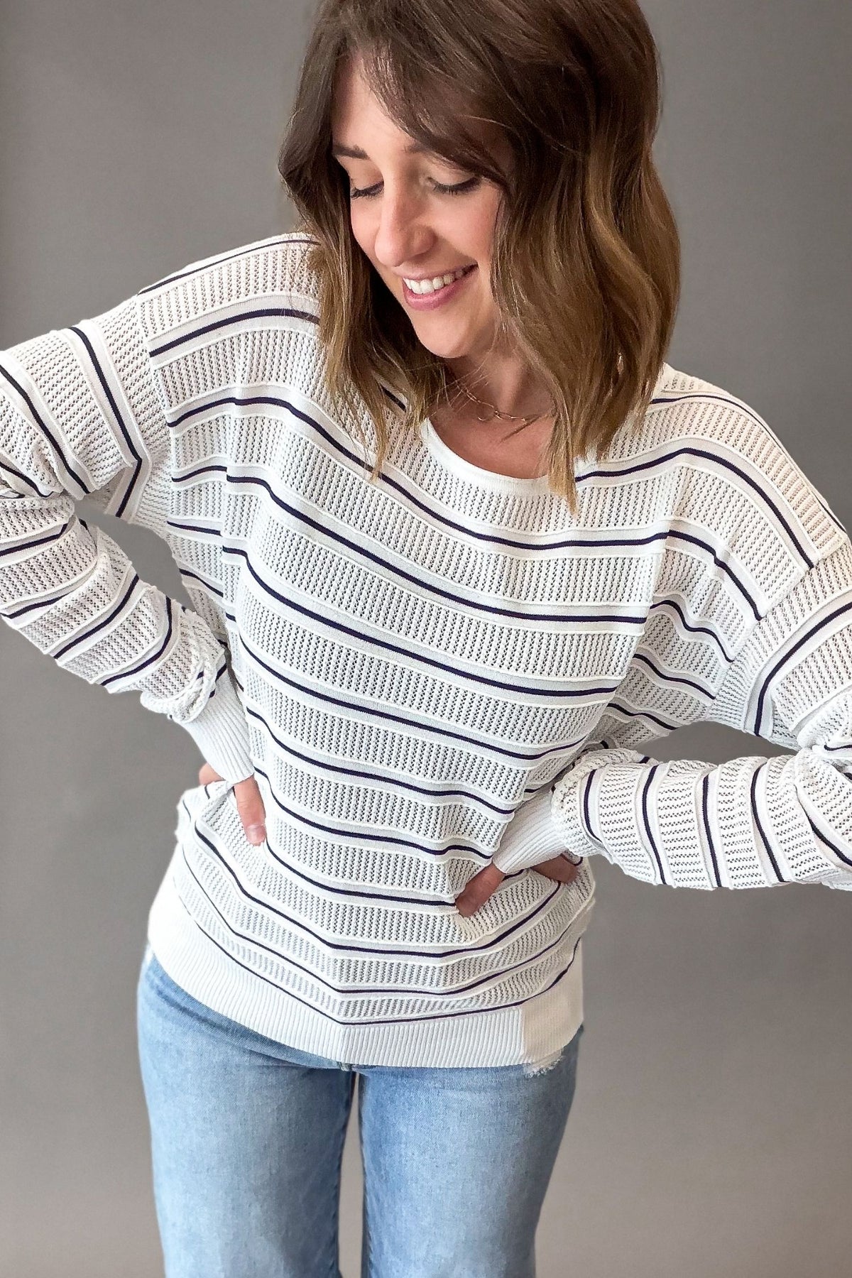 woman wearing a white pullover with navy stripes with blue jeans on a grey background