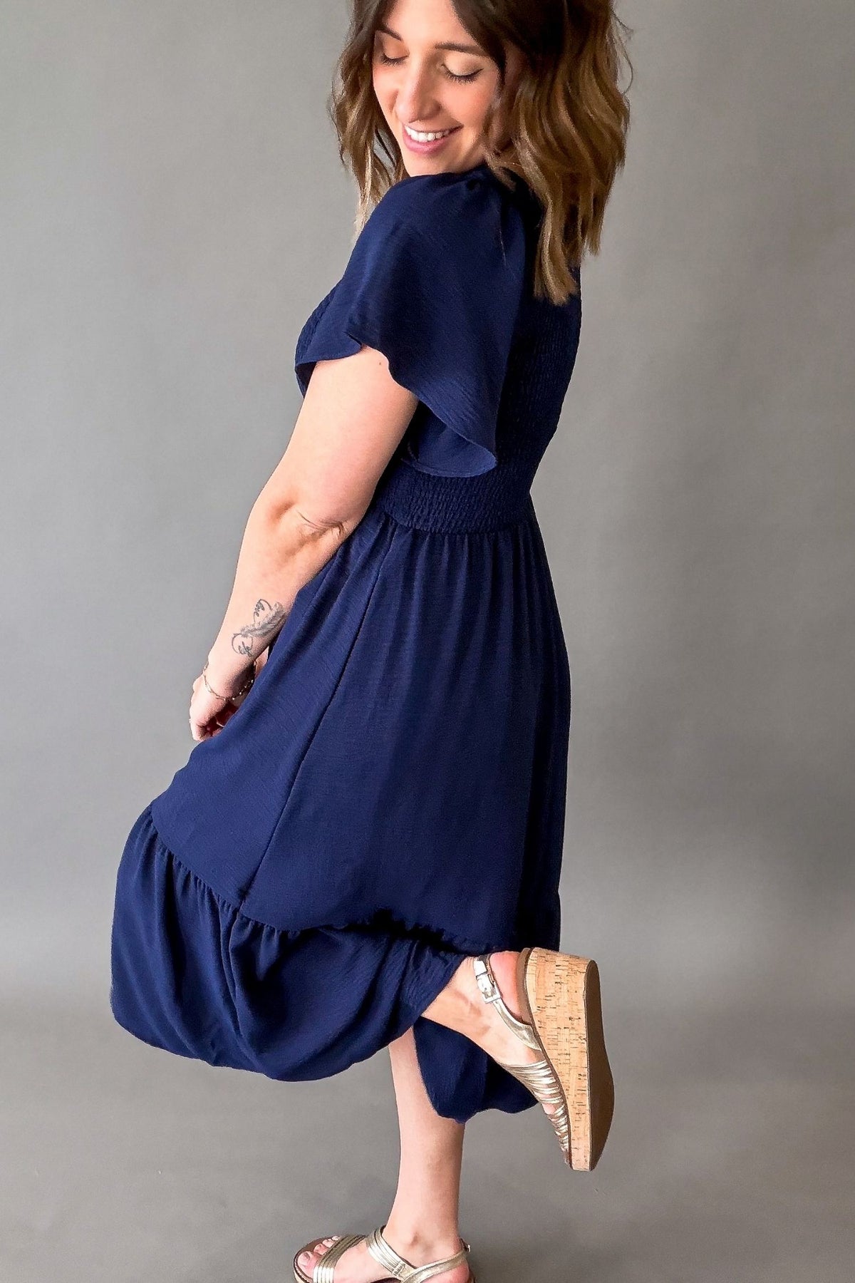 Woman wearing a navy blue dress on a gray background shwoing the side and back details