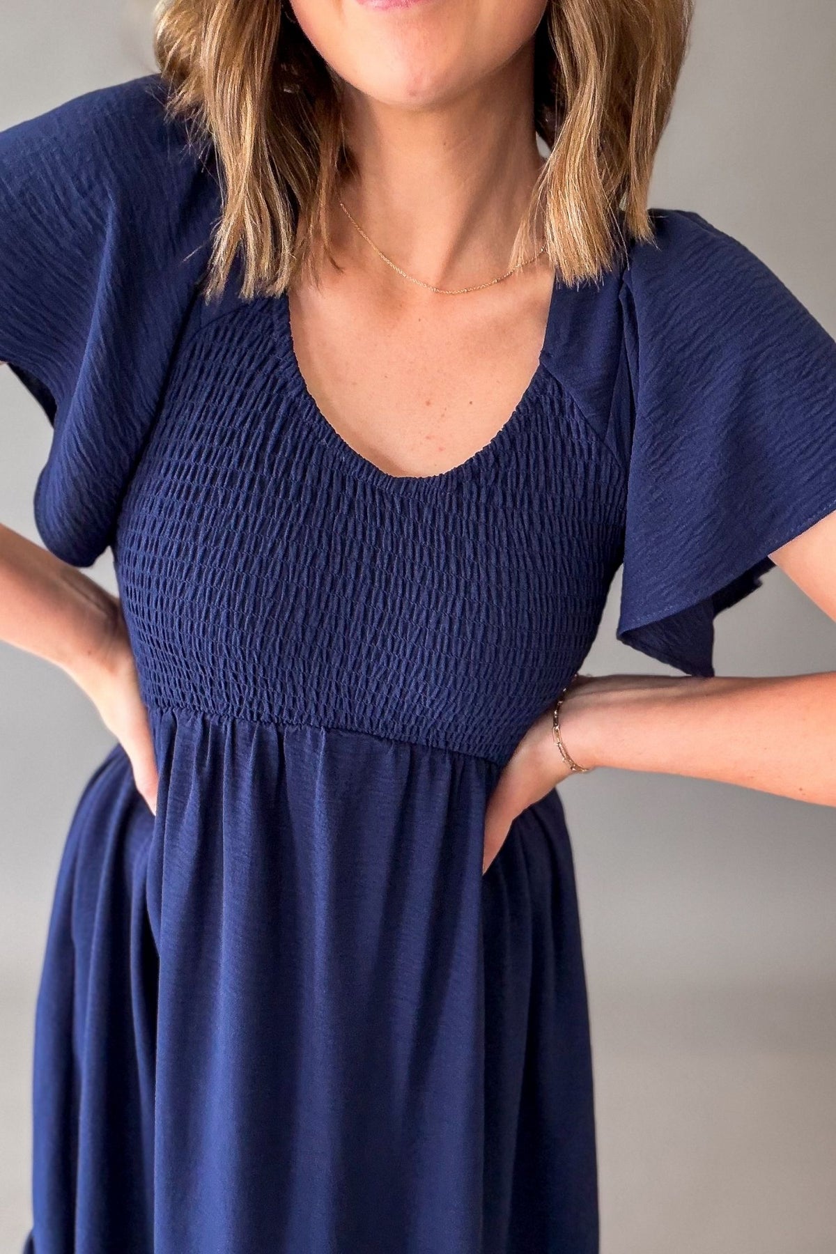 Woman wearing a navy blue dress with a plain background showing close up details of slight texture and smocking.