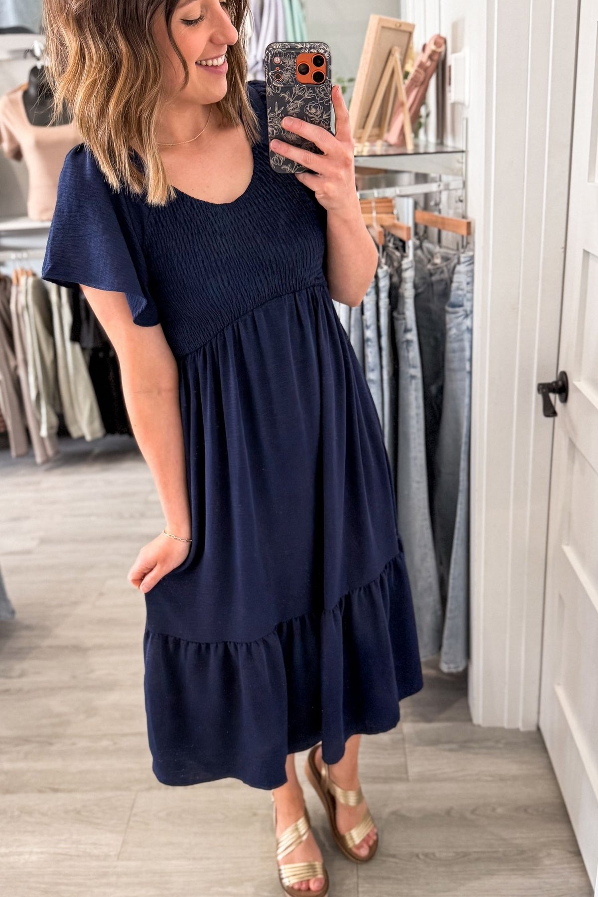 Woman taking a mirror selfie wearing a navy blue dress in a clothing store.