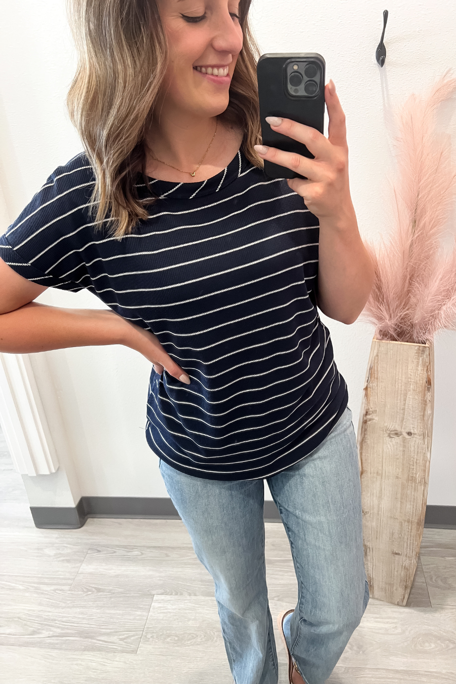 Woman taking a mirror selfie wearing a navy and white striped t-shirt and light blue jeans.