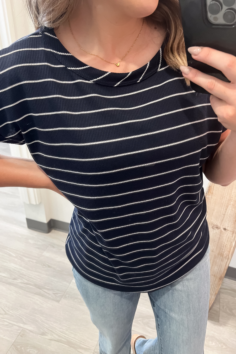 Person wearing a navy blue and white striped shirt with light blue jeans indoors.