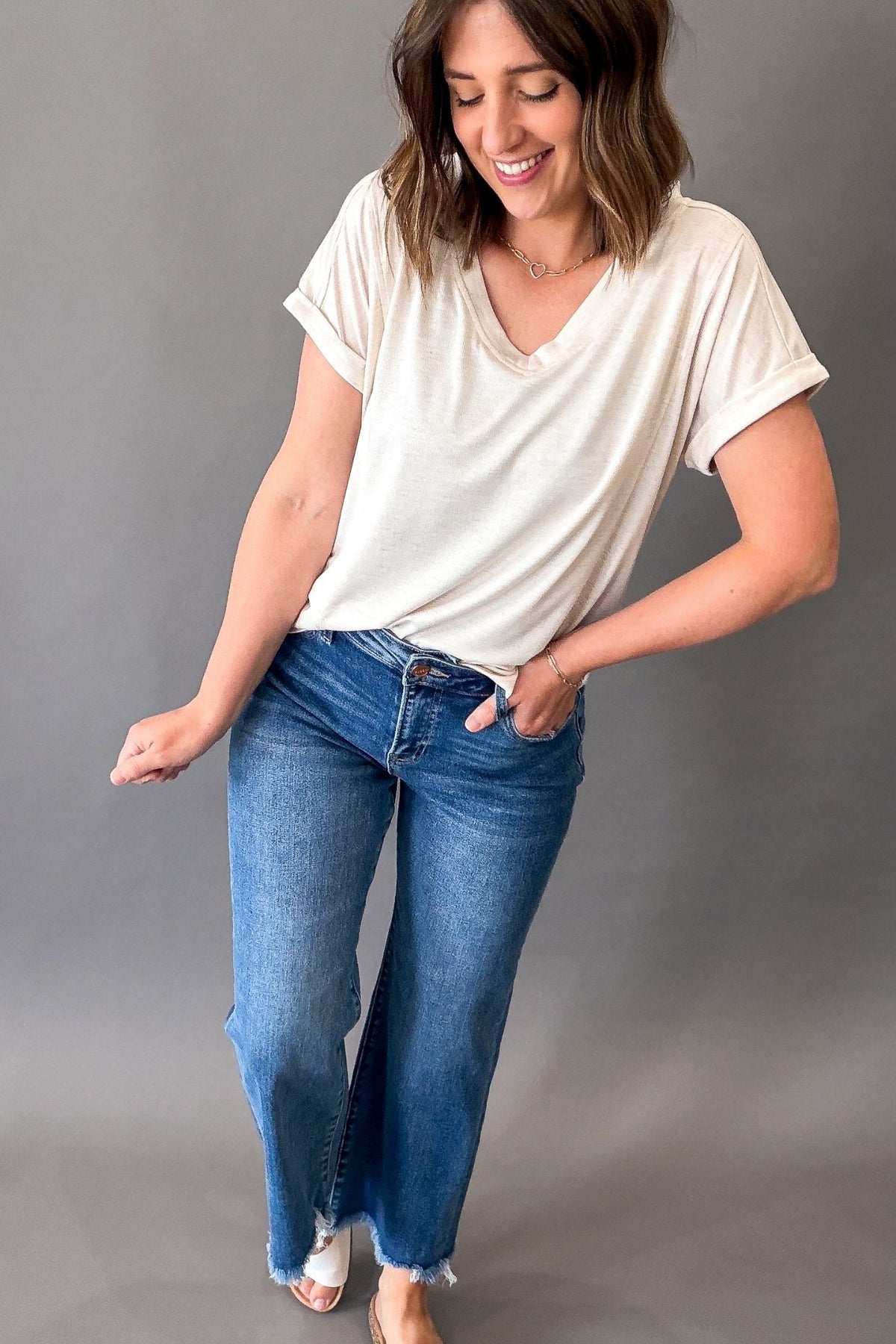 Woman wearing a oatmeal striped t-shirt and blue jeans against a gray background