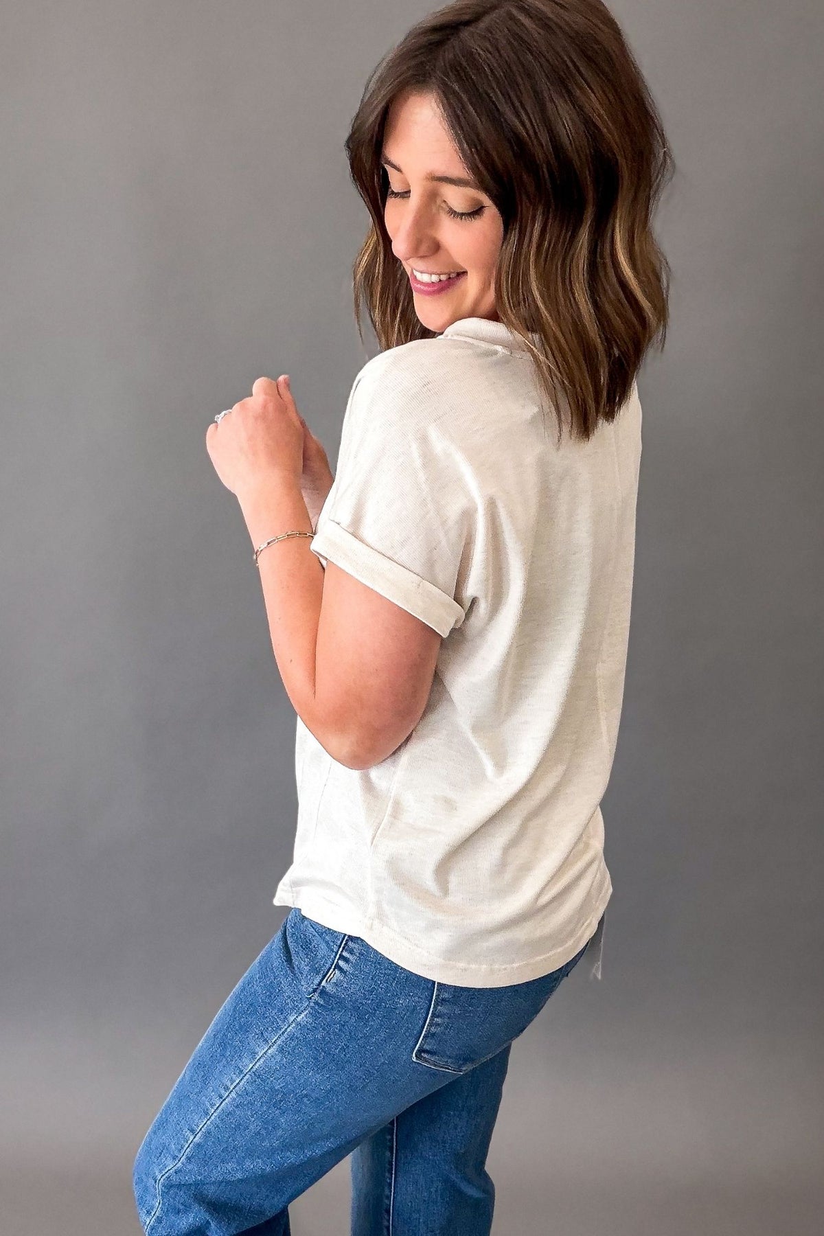 Woman wearing a oatmeal shirt and blue jeans against a gray background