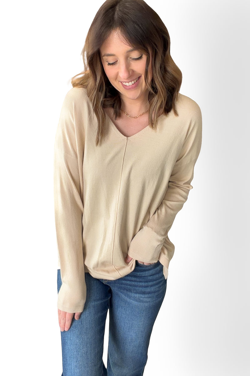 Woman wearing a oatmeal long-sleeve top and blue jeans on a white background