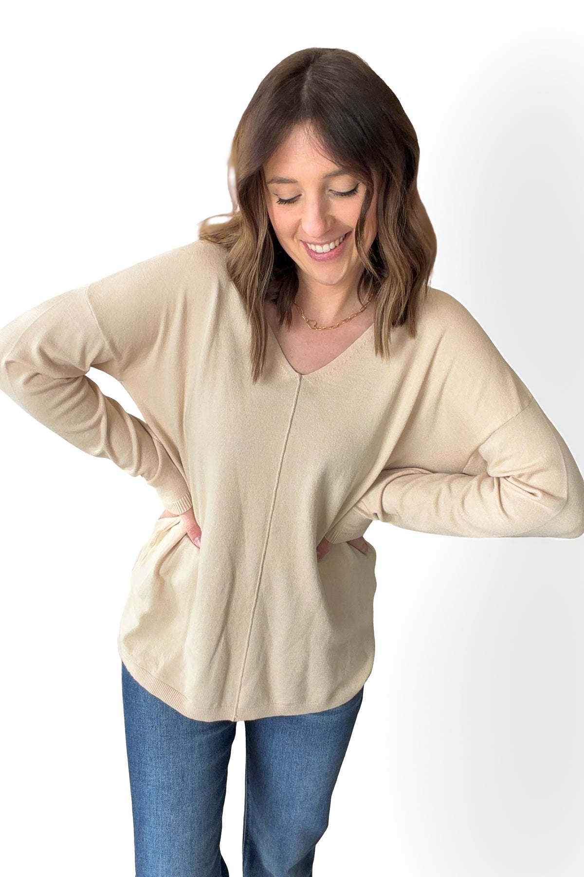 Woman wearing a oatmeal long-sleeve top and blue jeans on a white background