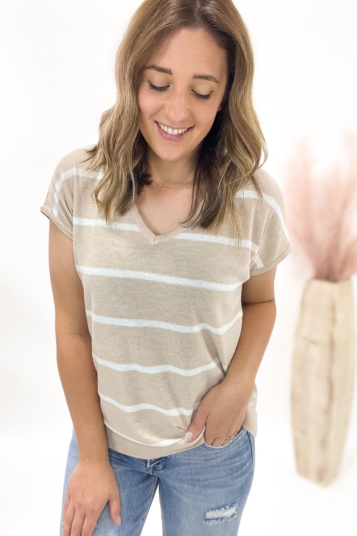 Woman wearing a beige and white striped t-shirt with blue jeans on a plain background