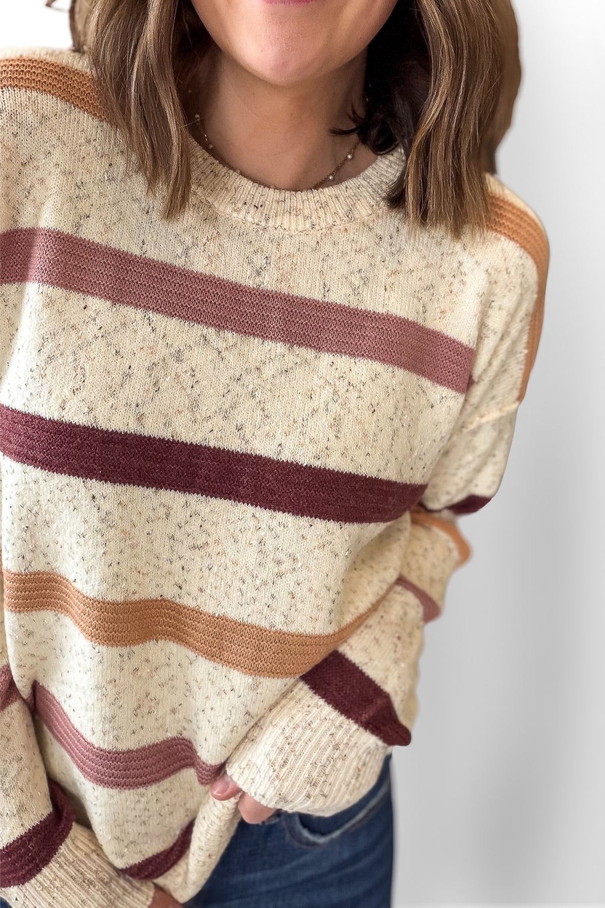 Person wearing a cream sweater with brown and red horizontal stripes on a plain background