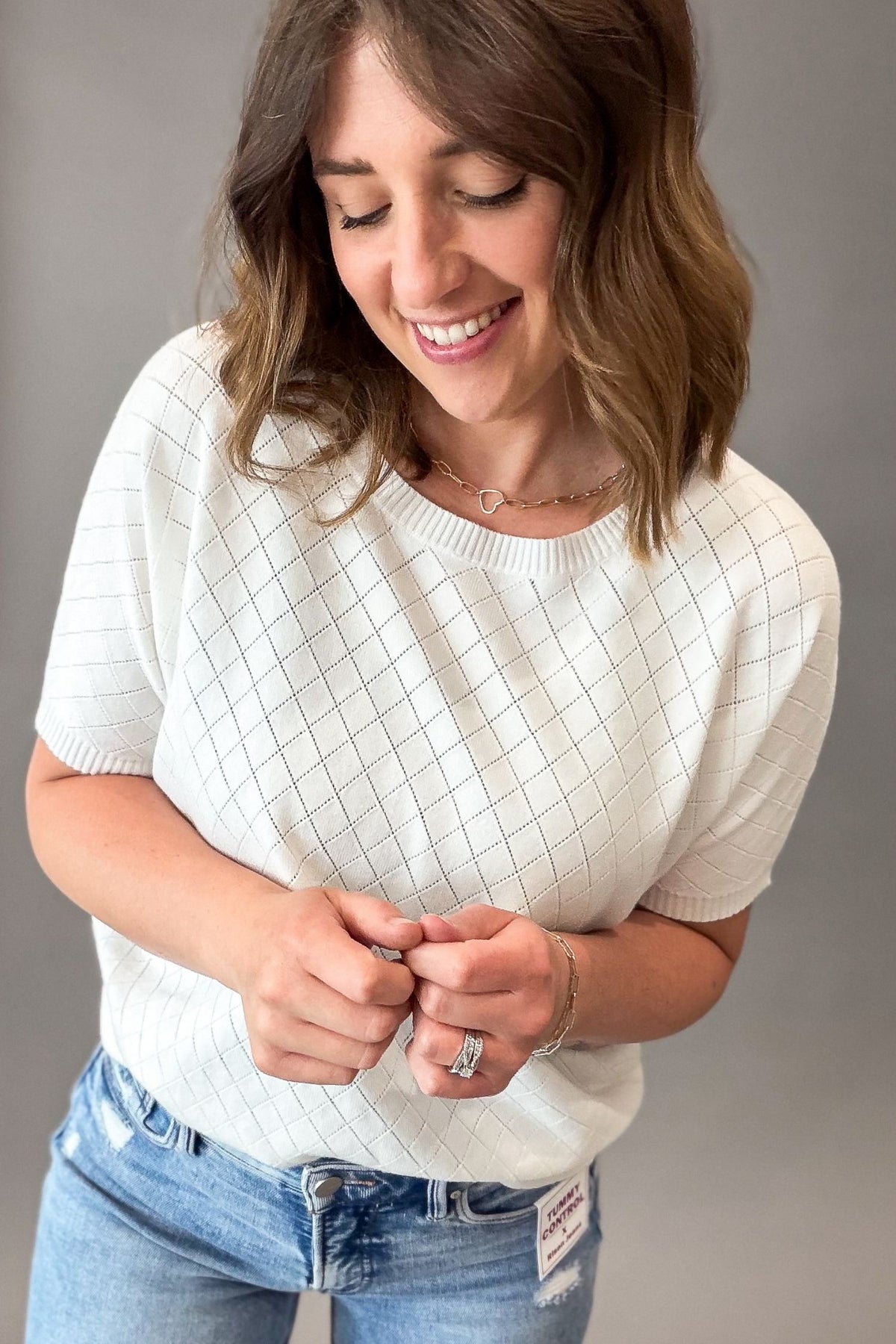 Woman wearing a white textured sweater and blue jeans against a gray background