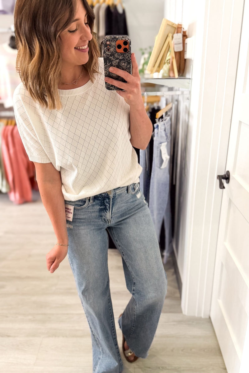 Woman taking a mirror selfie wearing a white top and blue jeans in a clothing store.