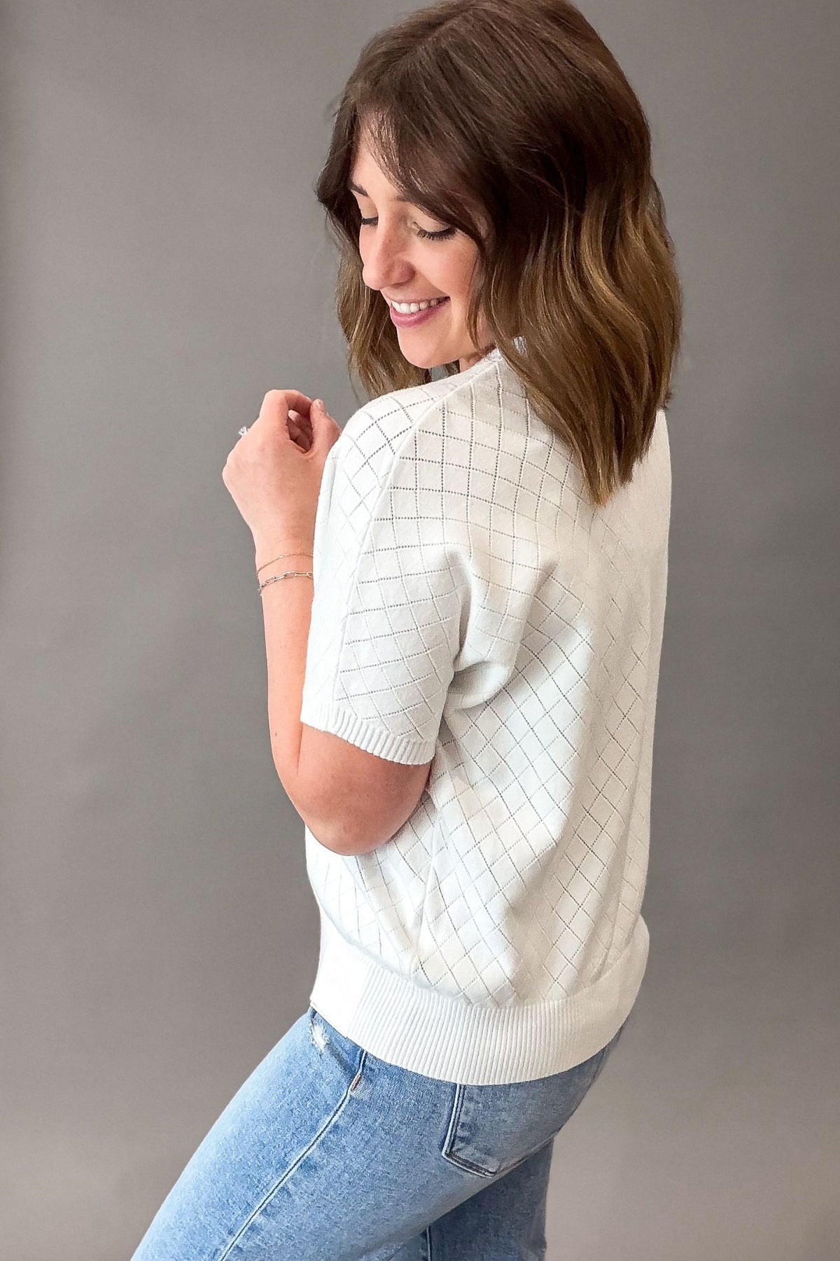 Woman wearing a white short-sleeve sweater and blue jeans against a gray background