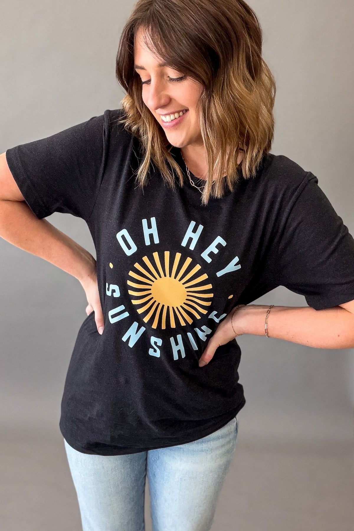 Woman wearing a black Oh Hey Sunshine graphic tee with yellow sun graphic and relaxed casual summer outfit showing the tee length.