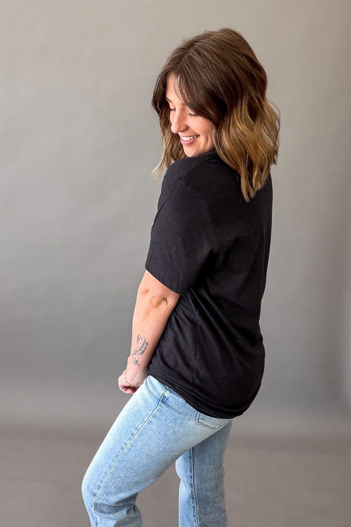  Woman wearing a black Oh Hey Sunshine graphic tee with yellow sun graphic and relaxed casual summer outfit showing the blank back details