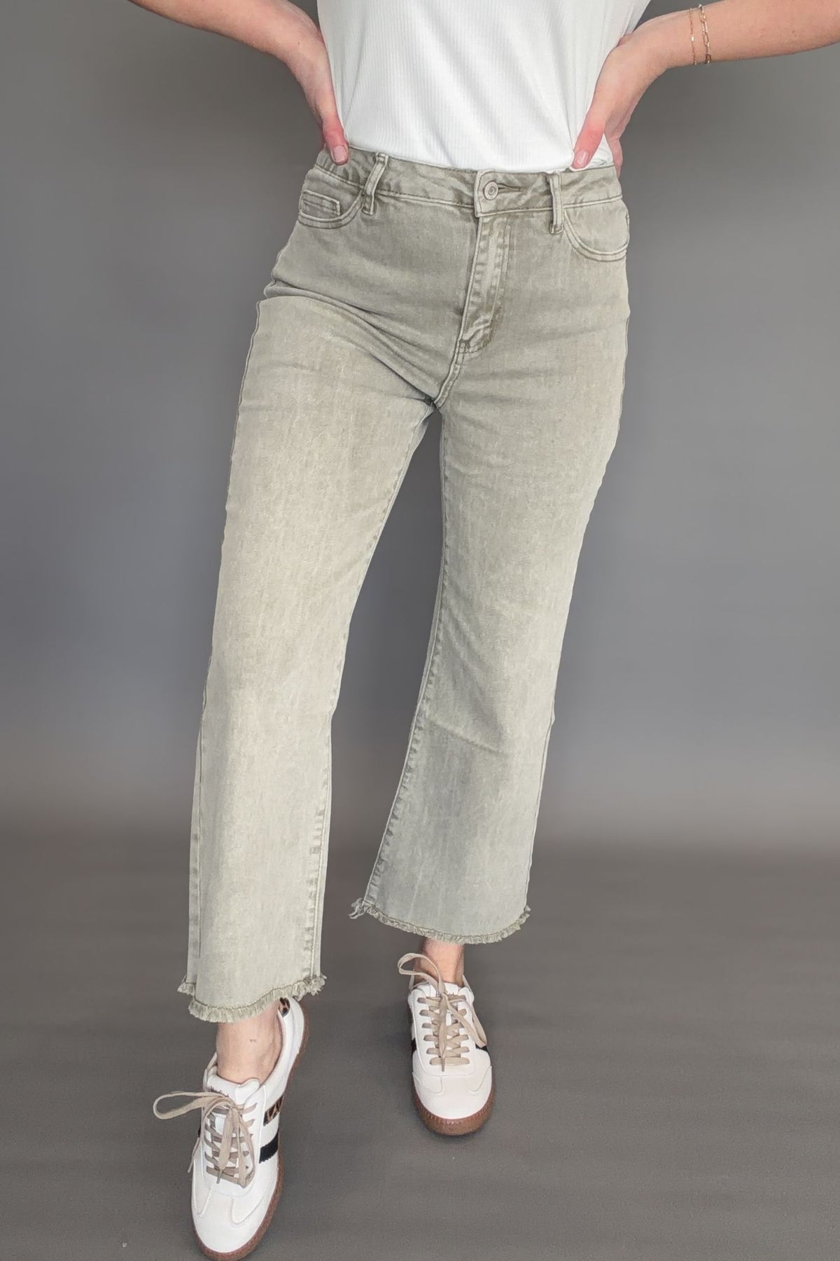 Front view of olive high rise crop bootcut jeans with frayed hem styled with sneakers.