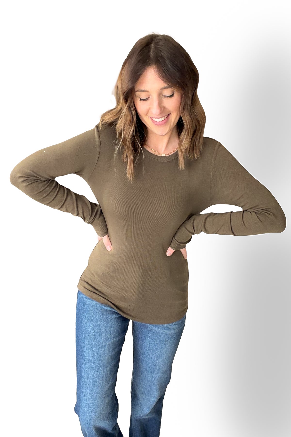 Woman wearing a olive long-sleeve top and blue jeans on a white background