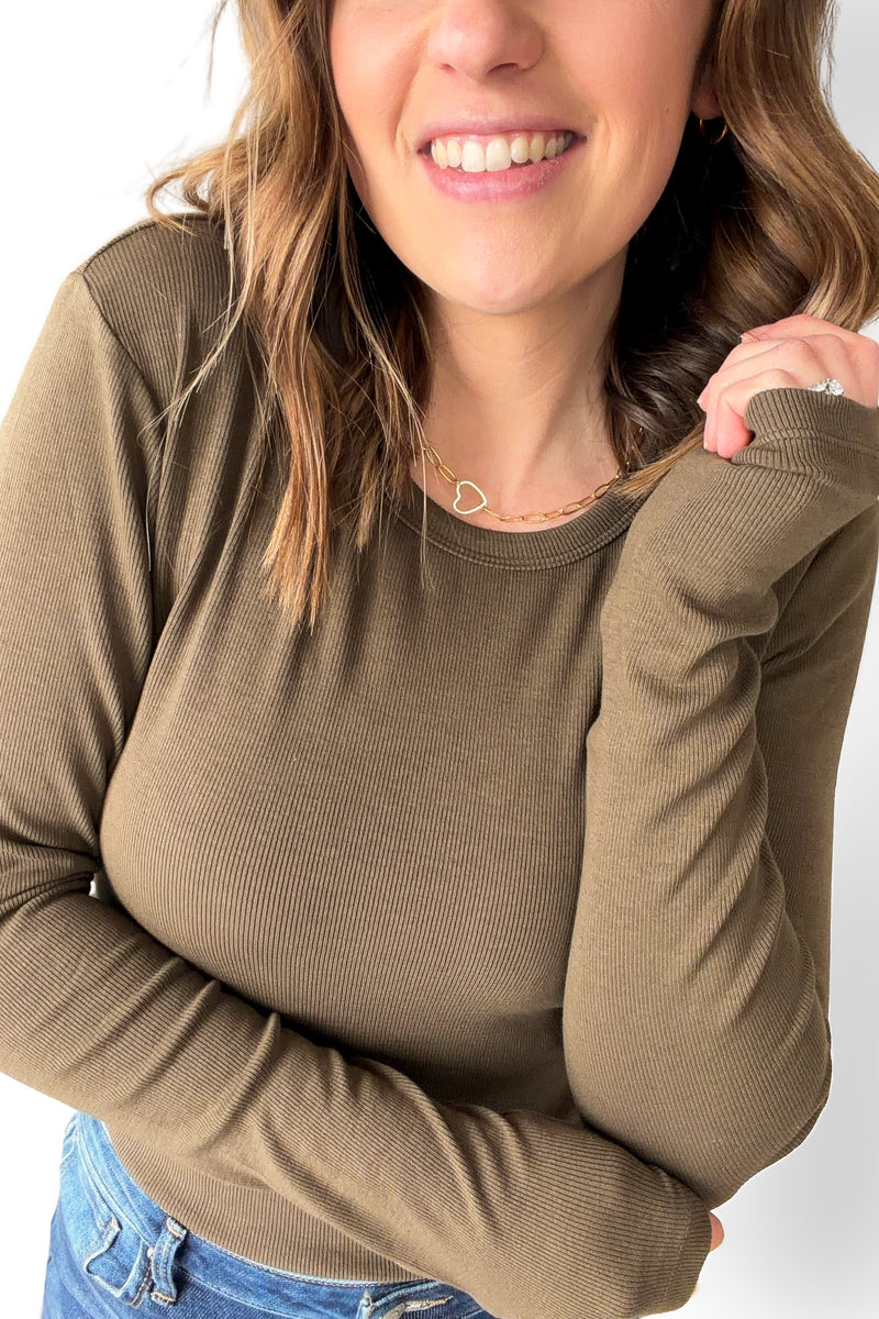 Woman wearing a olive long-sleeve top with a plain background up close showing ribbed texture
