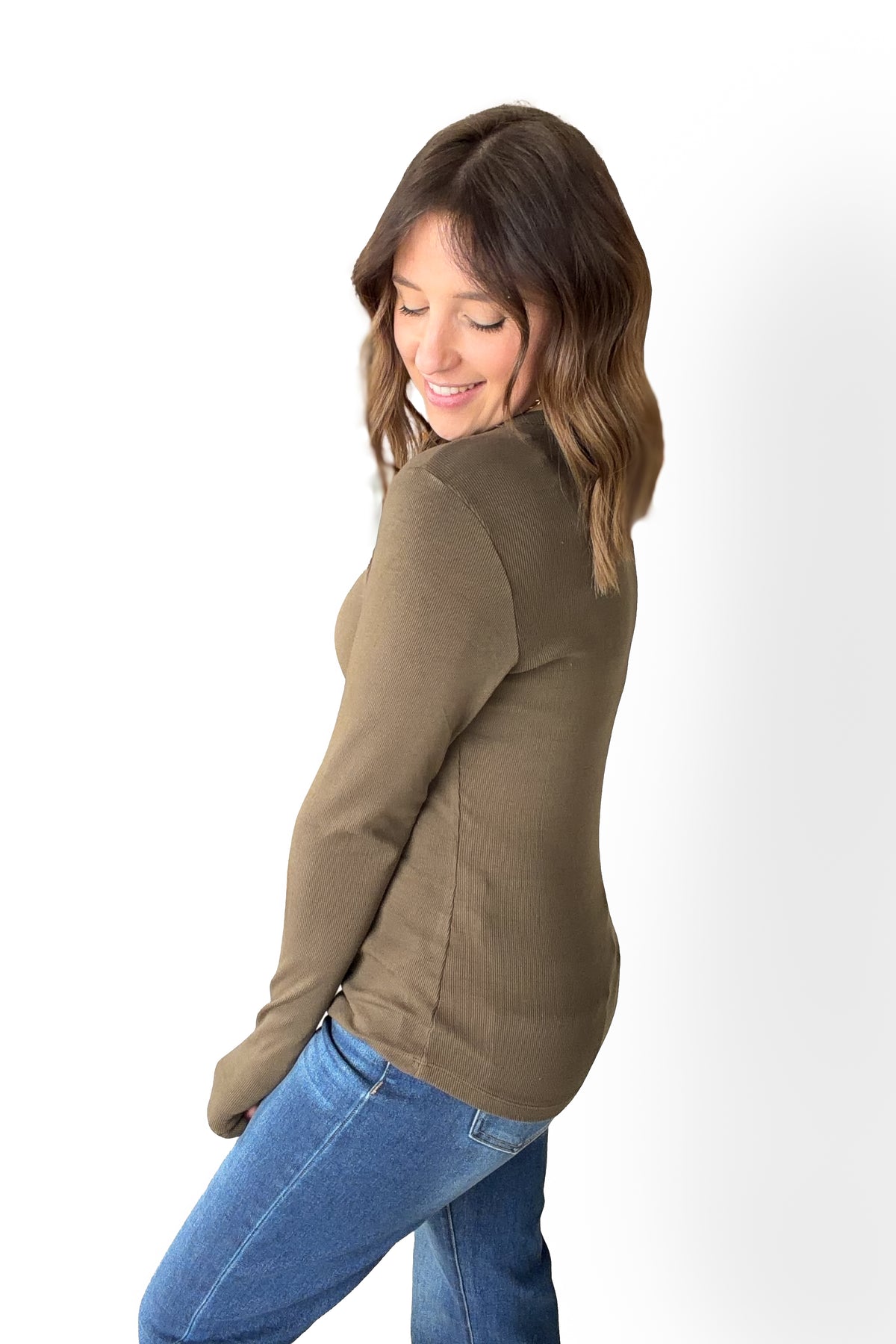Woman wearing a olive long sleeve fitted top showing the side view