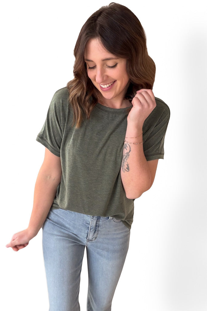 Woman wearing an olive short sleeve tee thats tucked in with blue jeans on a white background