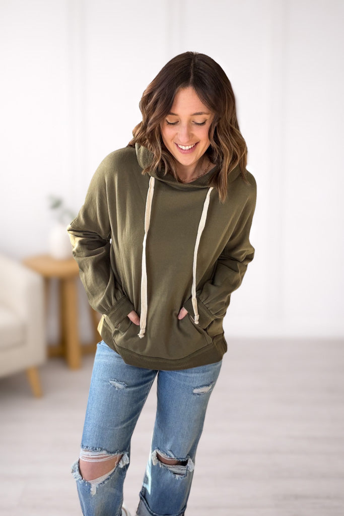 Woman wearing an olive green hoodie and ripped jeans indoors.