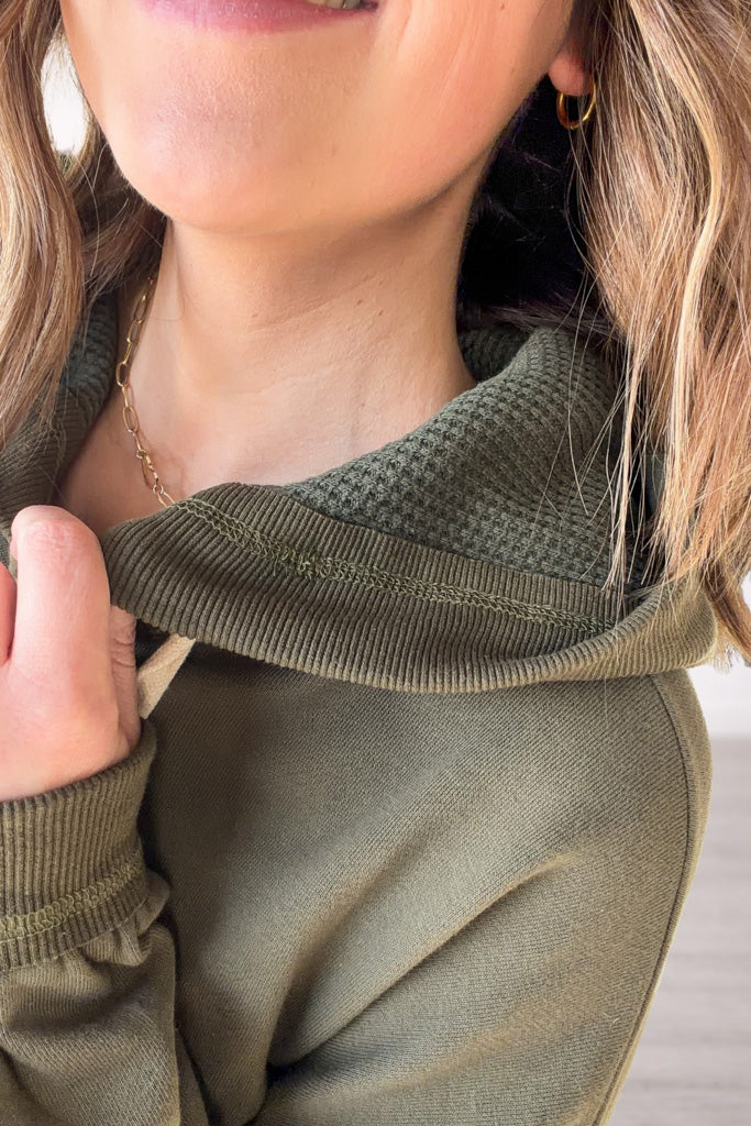 Close-up of a person wearing an olive green sweater with a blurred background