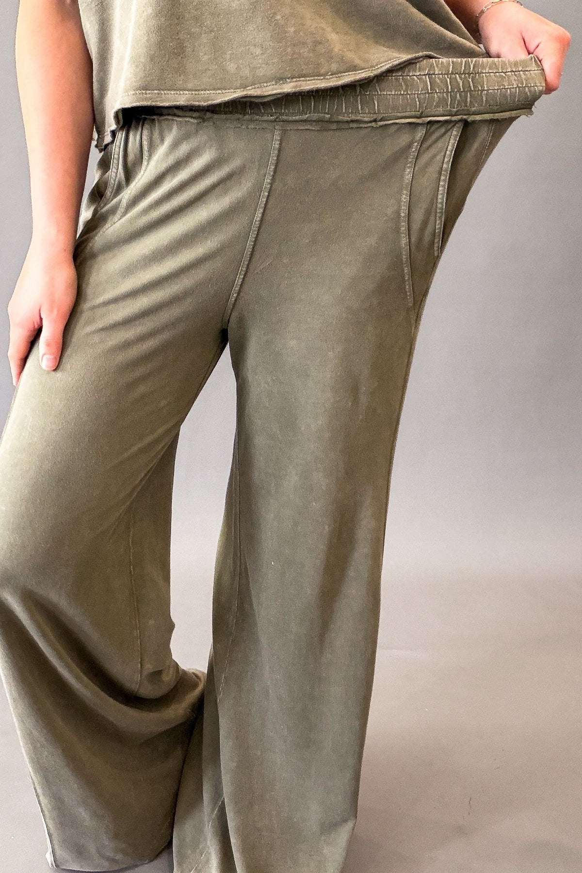 woman wearing olive lounge pants showing the stretch in the waistband.