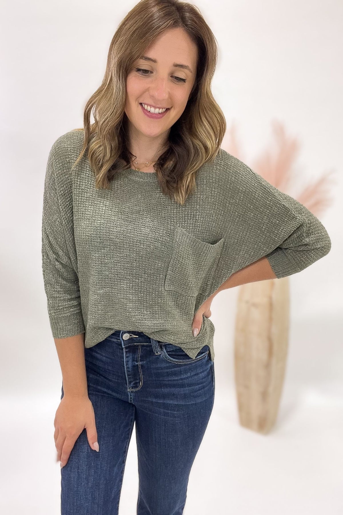 Woman wearing a green sweater and blue jeans against a white background
