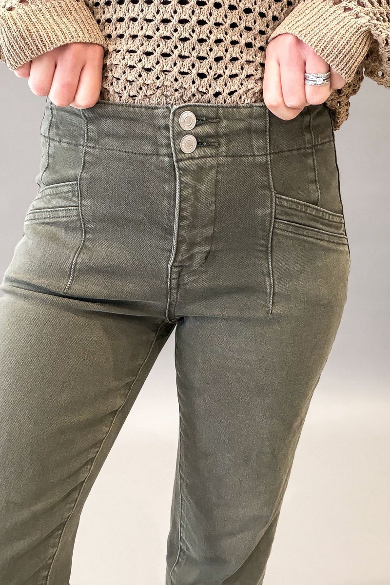 A close-up of a person wearing olive green high-waisted jeans with a double-button closure, paired with a beige knit sweater.