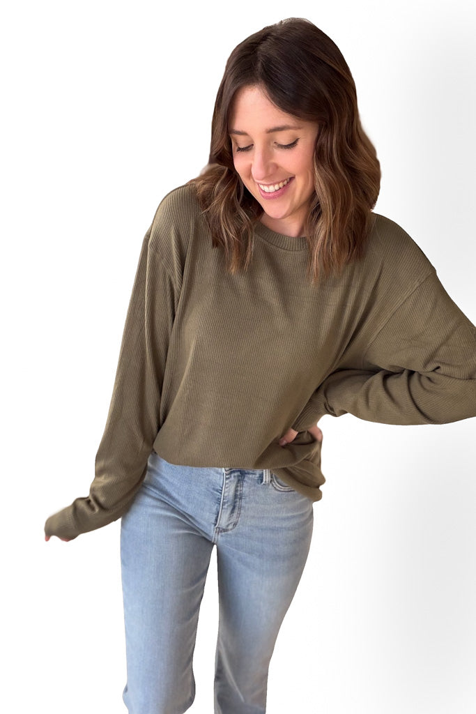 Woman wearing an olive long sleeve sweater with blue jeans against a white background