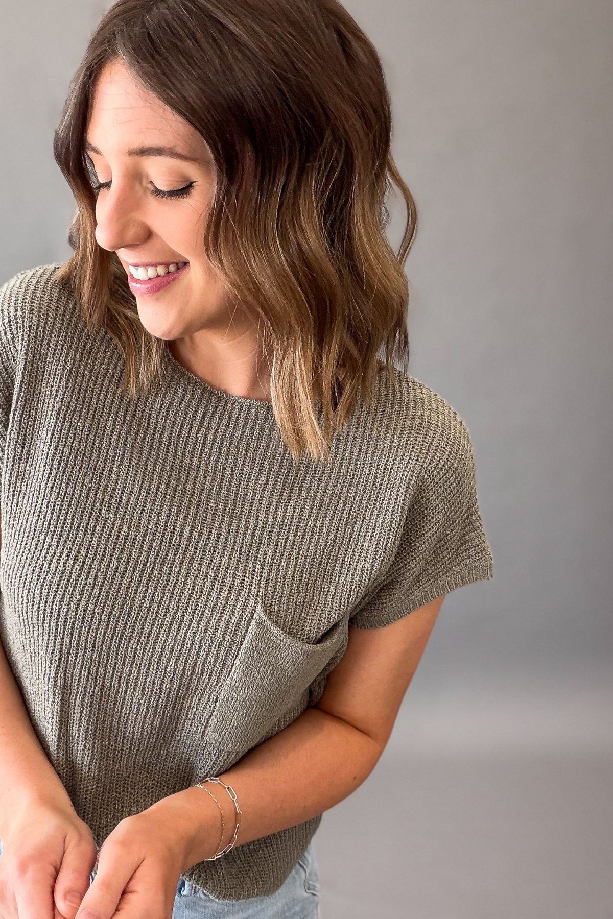 woman wearing a olive knit top with a chest pocket on a grey background