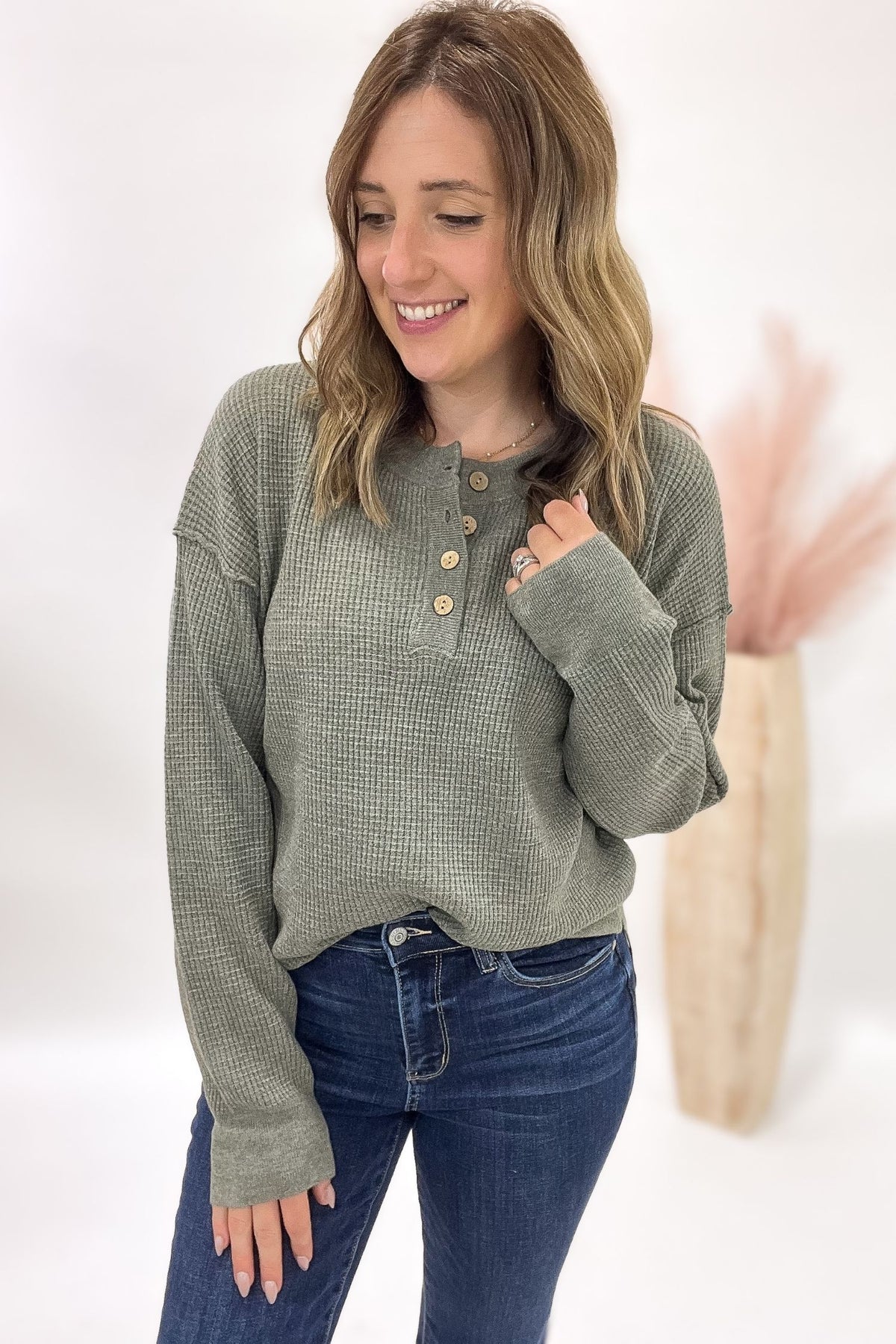 Woman wearing a green long-sleeve shirt with buttons and blue jeans on a white background