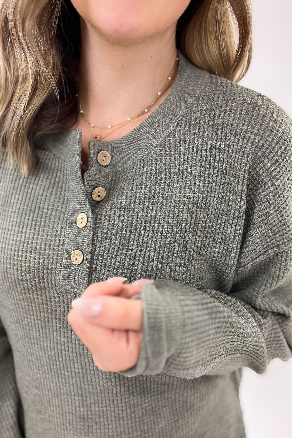 Person wearing a olive waffle textured sweater with buttons on a white background