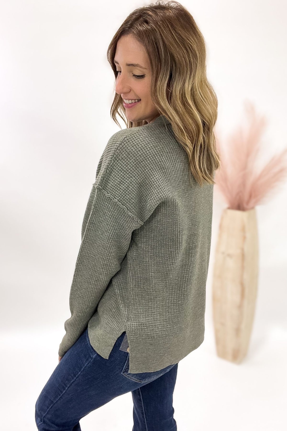 Woman wearing a green sweater and blue jeans against a white background