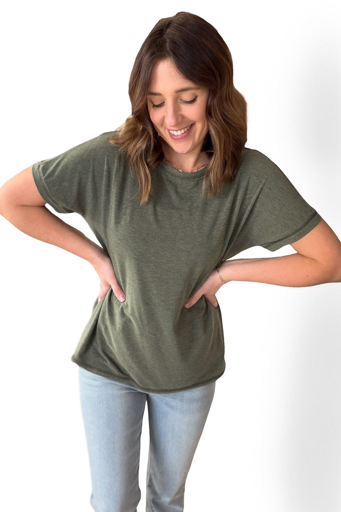 Woman wearing an olive short sleeve tee with blue jeans on a white background