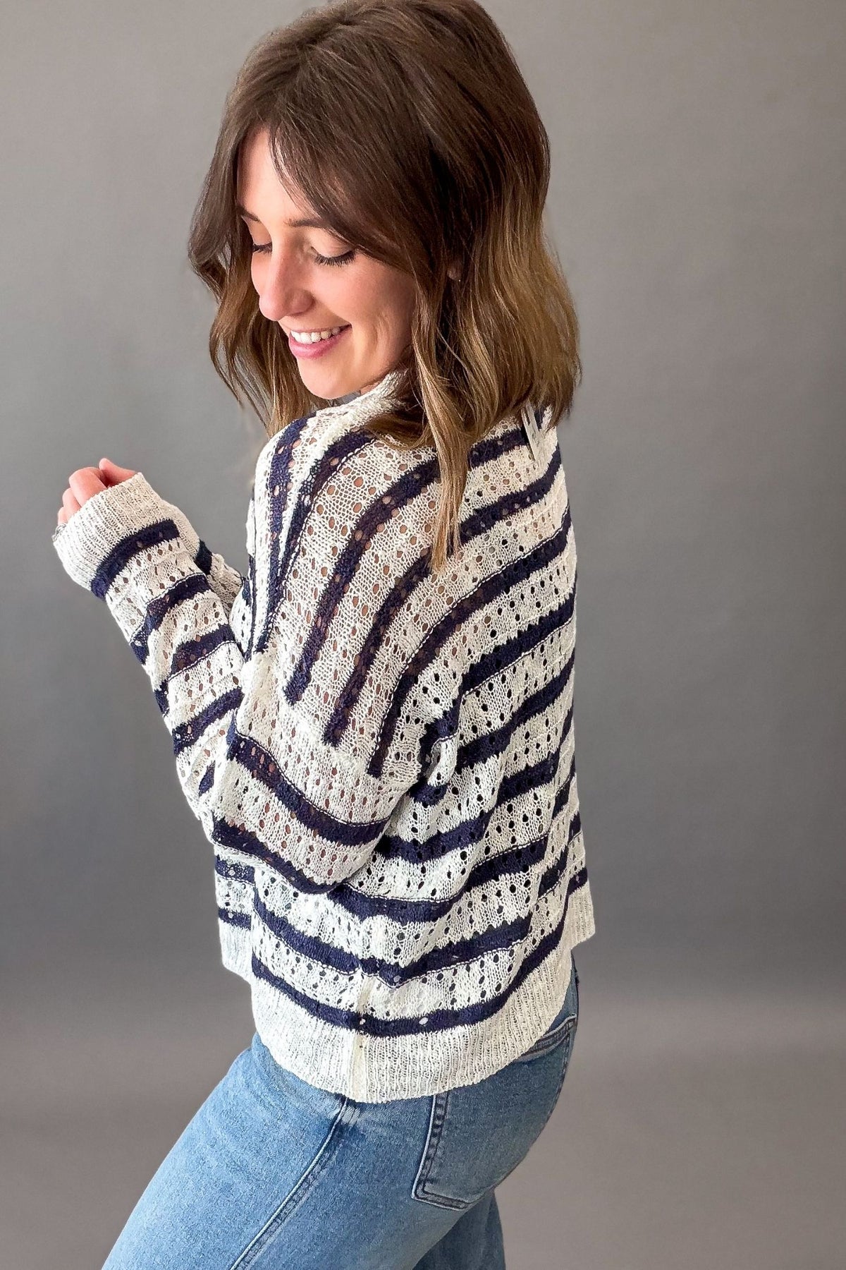 Woman wearing a striped sweater and jeans against a gray background