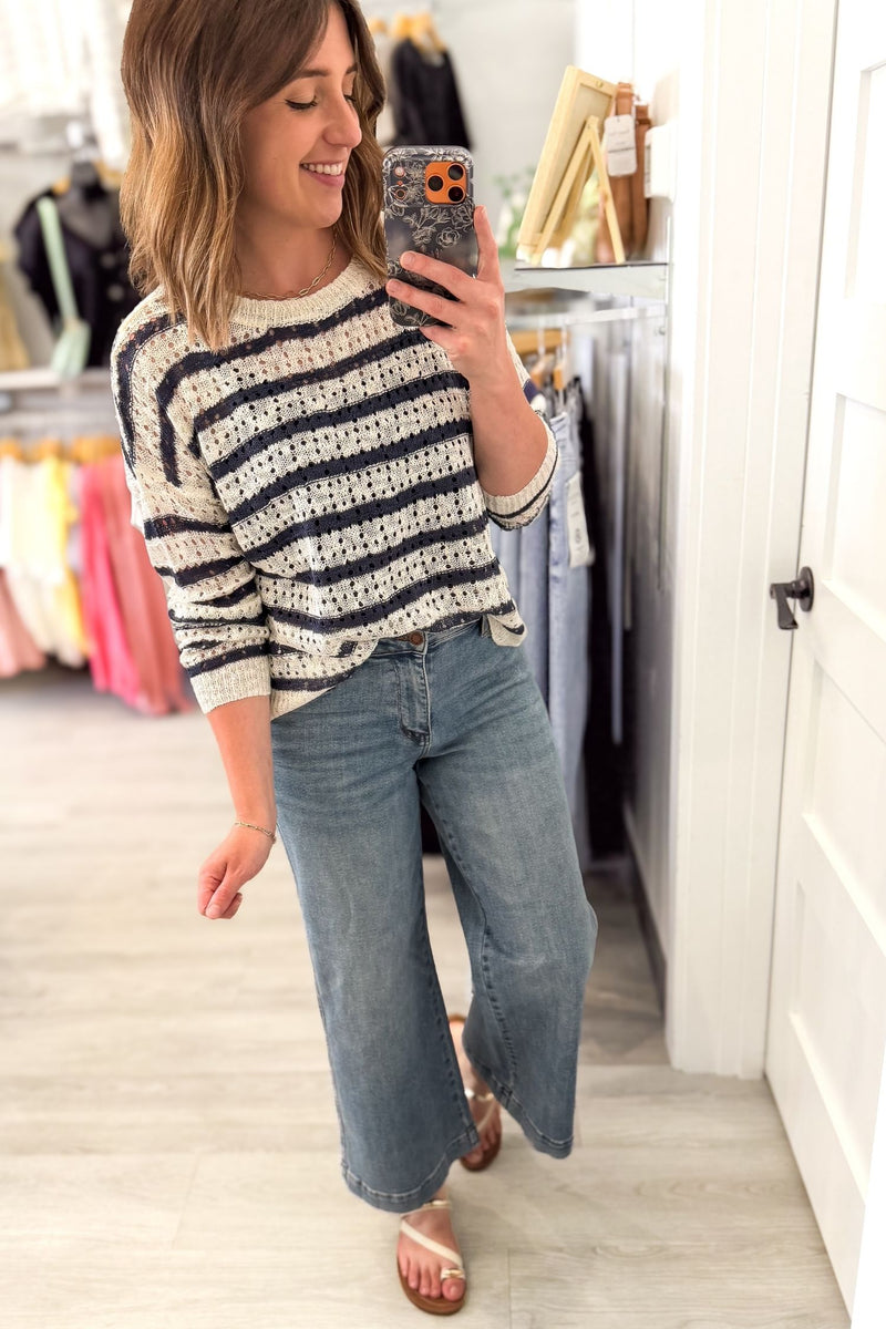 Woman taking a mirror selfie wearing a striped navy sweater and jeans in a store.