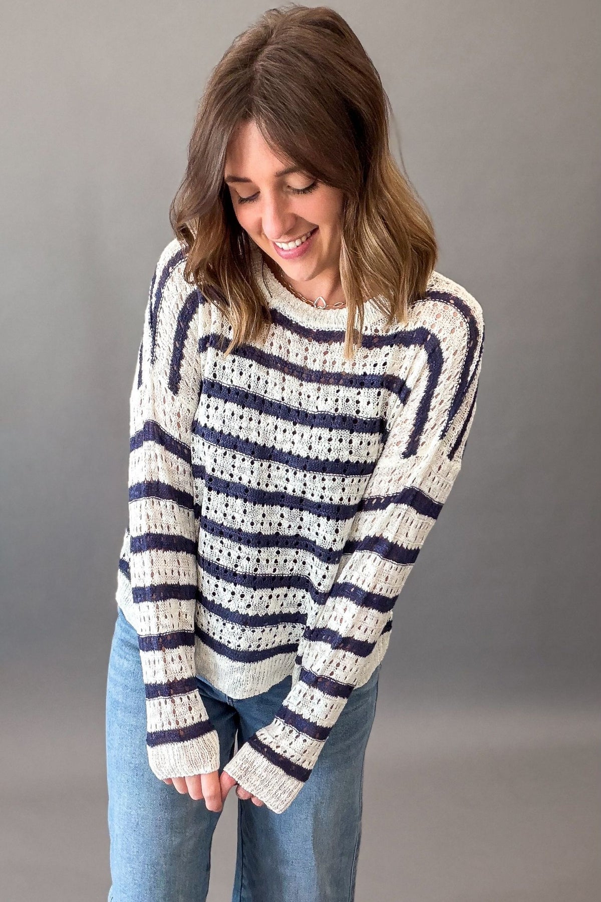 Woman wearing a striped sweater and jeans against a gray background