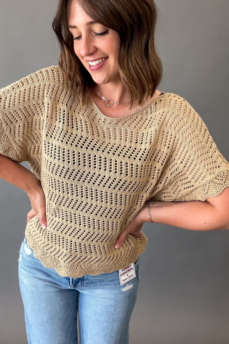 Woman wearing a lightweight latte open weave crochet sweater with short sleeves styled with light wash denim jeans.
