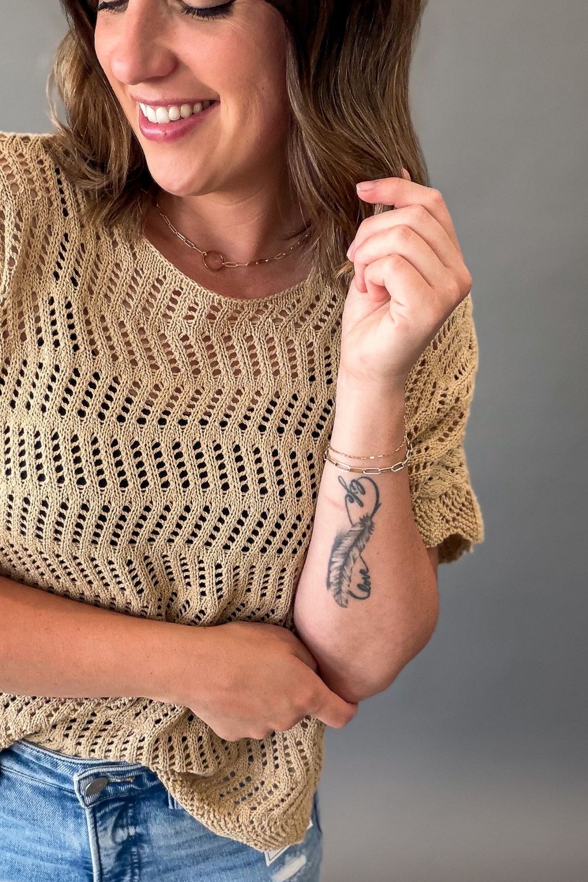 Woman wearing a lightweight latte open weave crochet sweater with short sleeves styled with light wash denim jeans showing upclose texture and knit