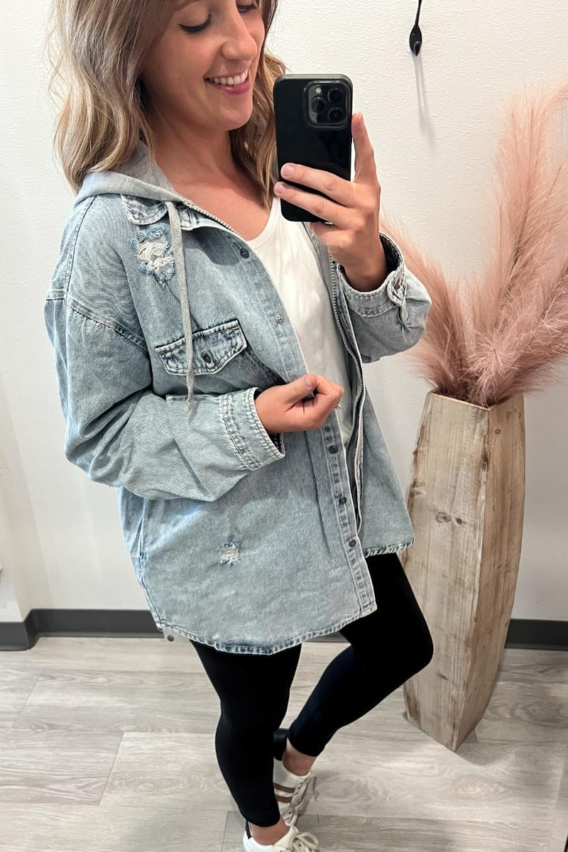 Woman taking a mirror selfie wearing a light blue denim jacket, white top, and black leggings.
