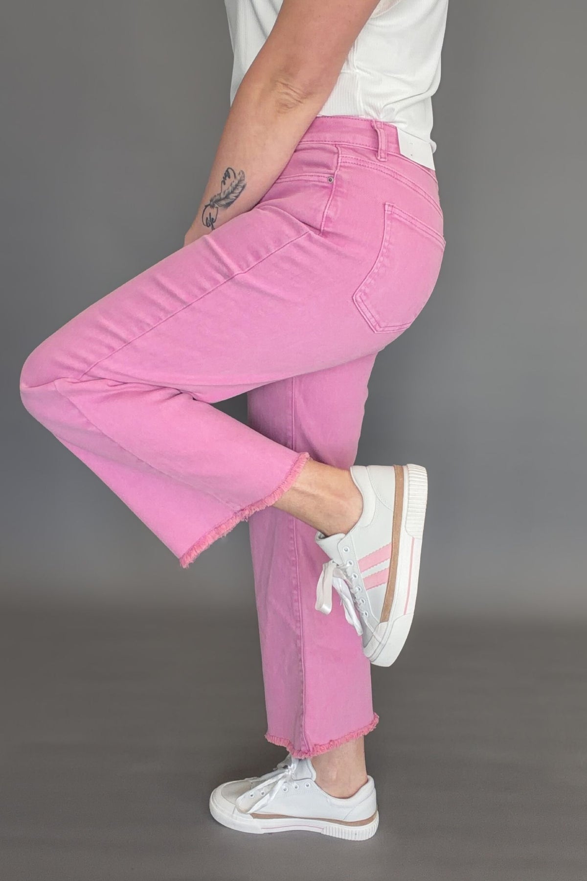 Side view of pink acid wash crop bootcut jeans with high rise fit and raw frayed hem detail.