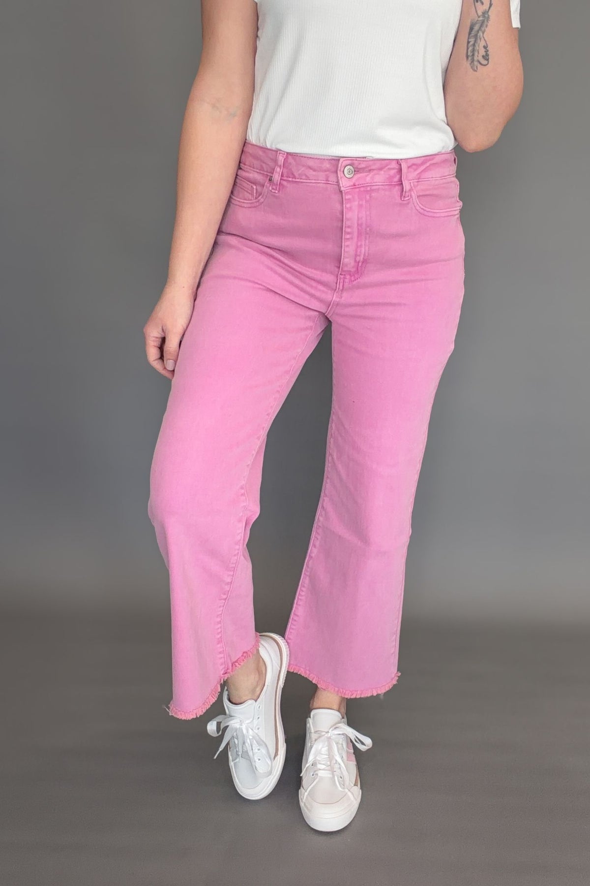 Pink acid wash high rise crop bootcut jeans with frayed hem styled on model, front view.