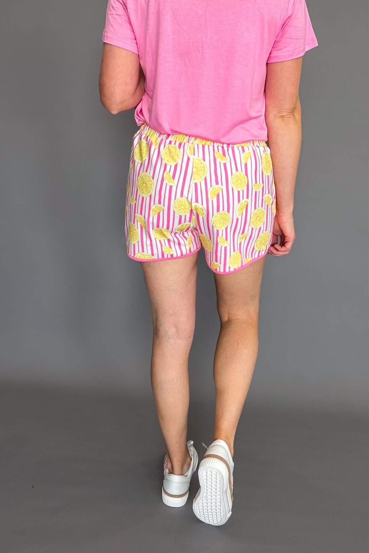 Pink lemon patterned soft stretchy everyday shorts with drawstring waist and pockets styled with sneakers showing the back details.